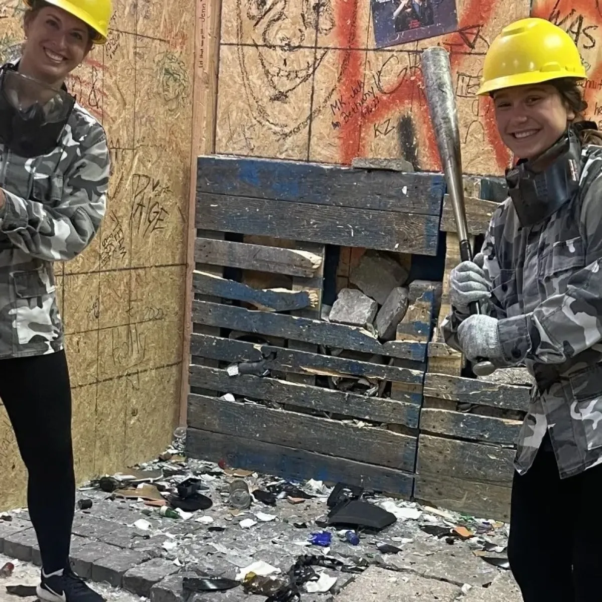 Two people in hard hats with bats in a graffiti-covered room.