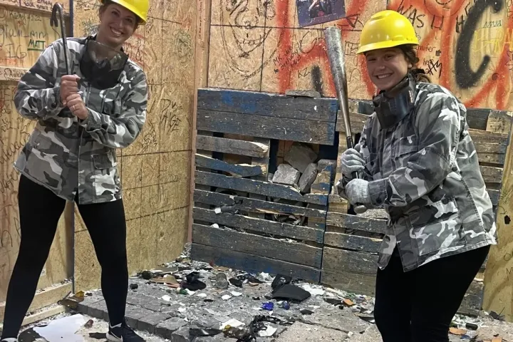 Two people in hard hats with bats in a graffiti-covered room.