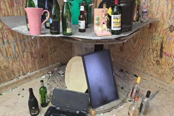 Collection of empty bottles and broken glass on a graffiti-covered table.