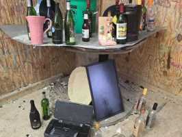 A cluttered corner with bottles, a green bucket, and an overturned monitor.