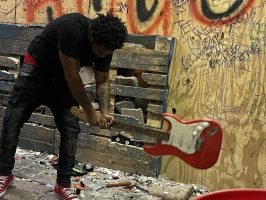 Person smashing guitar in graffiti-covered room.