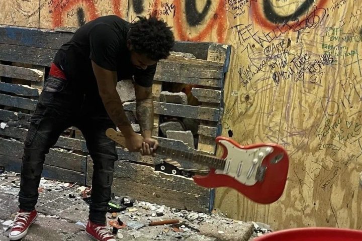 Person smashing guitar in graffiti-covered room.