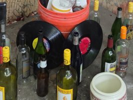 Graffitied corner with bottles, records, and mugs on a shelf.