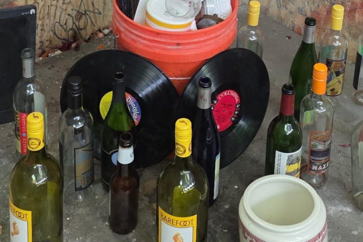 Graffitied corner with bottles, records, and mugs on a shelf.