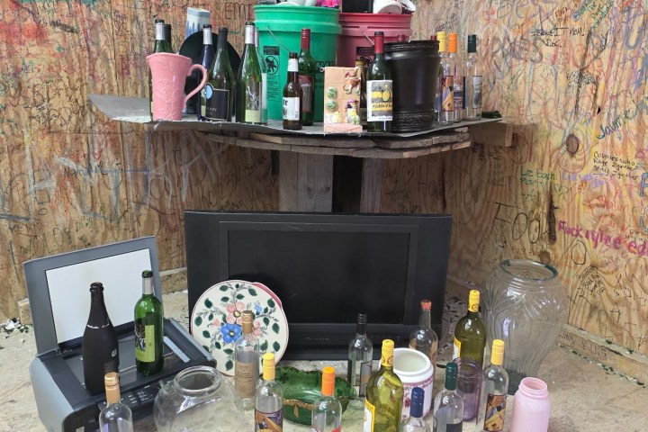 Assorted bottles and items on a graffiti-covered wooden shelf and floor.