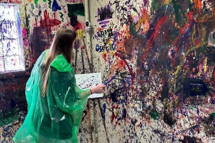 Person painting in a colorful room with paint splatters on walls.