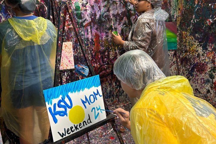 Three people in ponchos painting vibrantly splattered walls.